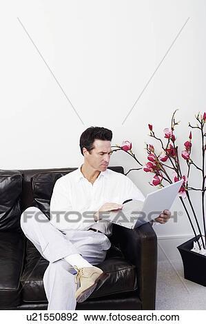 Stock Image - Mature man sitting on a couch and using a laptop. Fotosearch