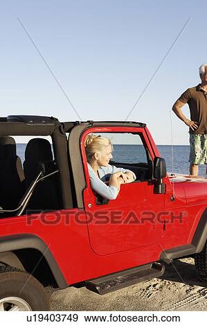 Mature woman sitting in a sports utility vehicle with a mature man standing with arms akimbo View Large Photo Image Stock Photo - Mature woman sitting in a sports utility vehicle with a mature man standing with arms akimbo. Fotosearch