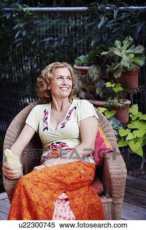 Stock Photography - Mature woman sitting in an armchair and holding a glass of lemonade. Fotosearch