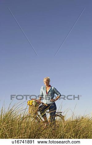 Mature woman standing in a field with a bicycle View Large Photo Image Stock Image - Mature woman standing in a field with a bicycle. Fotosearch