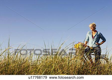 Mature woman standing in a field with a bicycle View Large Photo Image Stock Photo - Mature woman standing in a field with a bicycle. Fotosearch