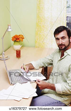 Portrait of a mature man sitting in front of a laptop and holding a document View Large Photo Image Stock Photo - Portrait of a mature man sitting in front of a laptop and holding a document. Fotosearch