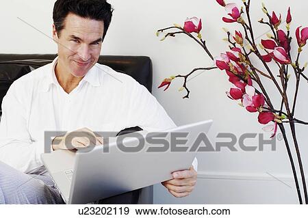 Stock Photo - Portrait of a mature man sitting on a couch and using a laptop. Fotosearch