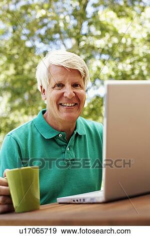 Portrait of a mature man smiling with a laptop in front of him View Large Photo Image Stock Photo - Portrait of a mature man smiling with a laptop in front of him. Fotosearch