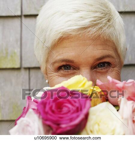 Portrait of a mature woman holding a bunch of flowers in front of her face View Large Photo Image Stock Image - Portrait of a mature woman holding a bunch of flowers in front of her face. Fotosearch