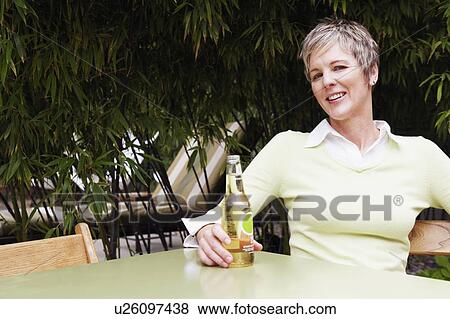 Portrait of a mature woman holding a bottle of wine and smiling View Large Photo Image Stock Photo - Portrait of a mature woman holding a bottle of wine and smiling. Fotosearch
