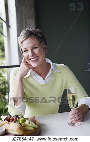 Stock Photo - Portrait of a mature woman holding a champagne flute and smiling. Fotosearch