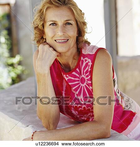 Portrait of a mature woman leaning against a wall with her hand on her chin and smiling View Large Photo Image Picture - Portrait of a mature woman leaning against a wall with her hand on her chin and smiling. Fotosearch