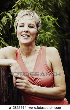 Picture - Portrait of a mature woman leaning against a fence and smiling. Fotosearch