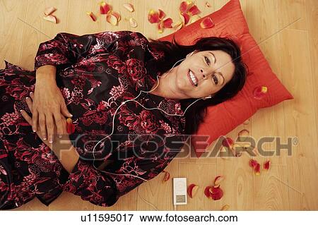 Portrait of a mature woman lying on the wooden floor and listening to an MP3 player View Large Photo Image Stock Photo - Portrait of a mature woman lying on the wooden floor and listening to an MP3 player. Fotosearch
