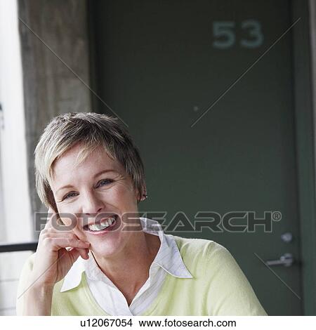 Picture - Portrait of a mature woman sitting at the table and smiling. Fotosearch