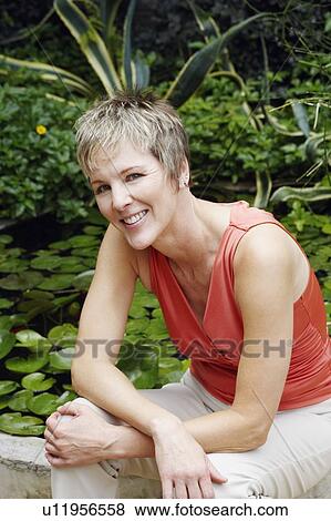 Portrait of a mature woman sitting on a ledge and smiling View Large Photo Image Stock Photo - Portrait of a mature woman sitting on a ledge and smiling. Fotosearch