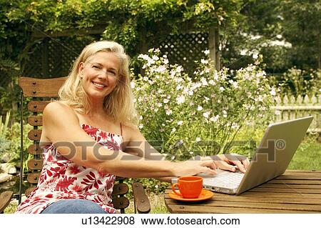 Stock Photo - Portrait of a mature woman sitting on a chair and using a laptop. Fotosearch