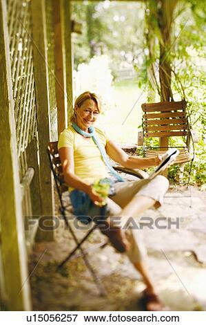 Stock Photo - Portrait of a mature woman sitting on a chair and holding a magazine. Fotosearch