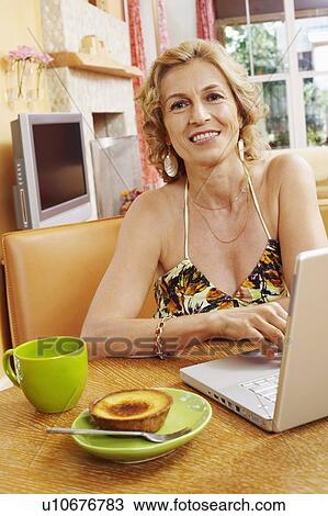 Stock Image - Portrait of a mature woman smiling in front of a laptop. Fotosearch