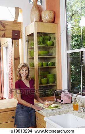Picture - Portrait of a mature woman standing in the kitchen and smiling. Fotosearch