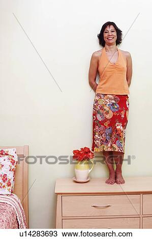 Portrait of a mature woman standing on a cabinet and smiling View Large Photo Image Stock Image - Portrait of a mature woman standing on a cabinet and smiling. Fotosearch