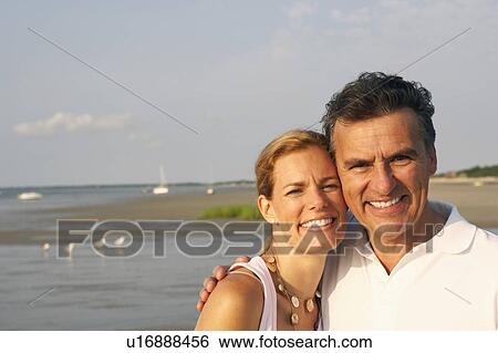 Stock Photograph - Portrait of a mid adult woman and a mature man standing on the beach and smiling. Fotosearch