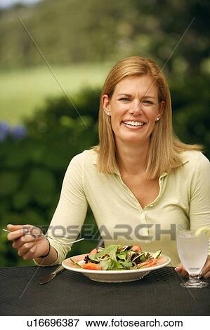 Stock Photo - Portrait of a mid adult woman sitting at a table with a plate of vegetable salad in front of her. Fotosearch