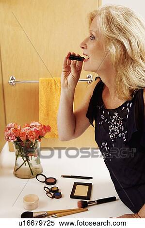 Stock Photography - Side profile of a mature woman applying lipstick in the bathroom. Fotosearch