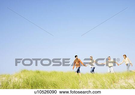 Stock Image - Two mature couples holding hands and walking on the beach. Fotosearch