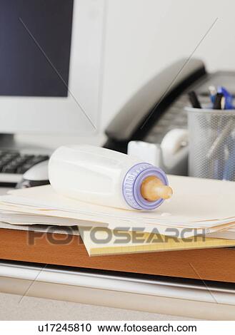 Stock Image - Baby bottle on desk of working mother in office. Fotosearch