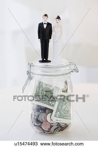 Stock Image - Bride and groom cake toppers on jar of money. Fotosearch