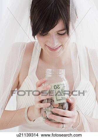 "Bride holding jar of money, studio shot" View Large Photo Image Picture - "Bride holding jar of money, studio shot". Fotosearch