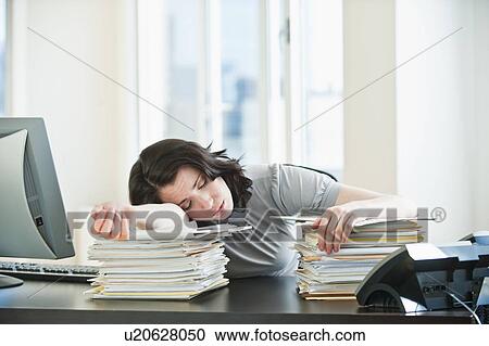 Stock Image - Business woman sleeping on paperwork at desk in office. Fotosearch