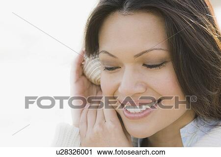 Stock Image - Close-up of woman listening to shell. Fotosearch