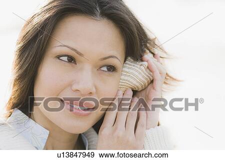 Stock Photo - Close-up of woman listening to shell. Fotosearch