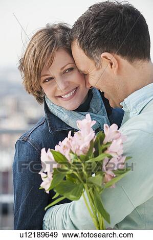 Stock Photo - "Couple embracing, woman holding flowers". Fotosearch