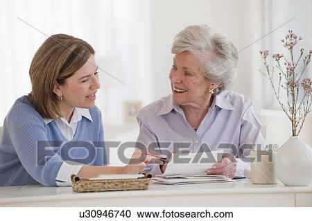 Stock Image - Daughter helping her mother paying bills. Fotosearch