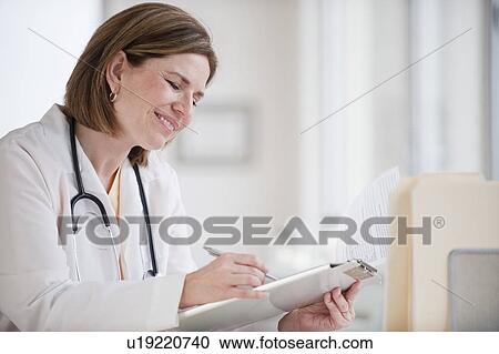 Stock Image - Female doctor writing on clipboard. Fotosearch