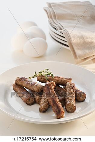 Picture - Fried sausages on plate with eggs and plates in background. Fotosearch