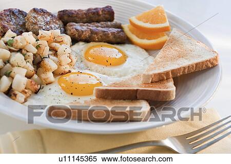 Stock Photography - Fried sausages on plate with eggs and plates in background. Fotosearch