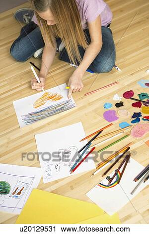 Stock Image - Girl (10-12) sitting on floor and drawing pictures. Fotosearch