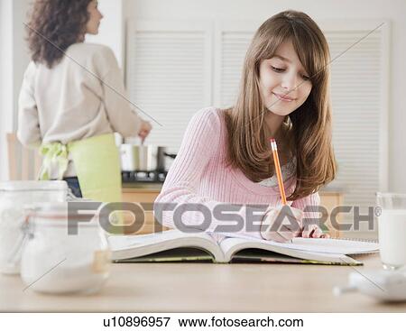 Girl (10-12 years) doing homework in kitchen while her mother is cooking View Large Photo Image Stock Photo - Girl (10-12 years) doing homework in kitchen while her mother is cooking. Fotosearch