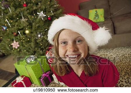 "Girl (9) wearing Santa hat sitting in front of Christmas tree, portrait" View Large Photo Image Stock Image - "Girl (9) wearing Santa hat sitting in front of Christmas tree, portrait". Fotosearch
