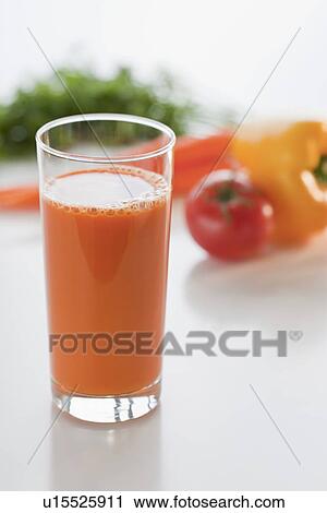 Stock Image - Glass of carrot juice with vegetable in background. Fotosearch