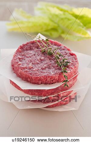 Stock Image - Hamburger patties in stack with salad leaves in background. Fotosearch