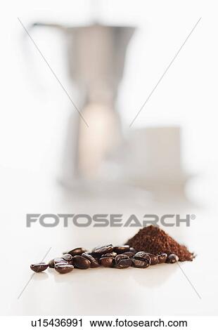 Stock Image - Heap of coffee beans with coffee cups in background. Fotosearch
