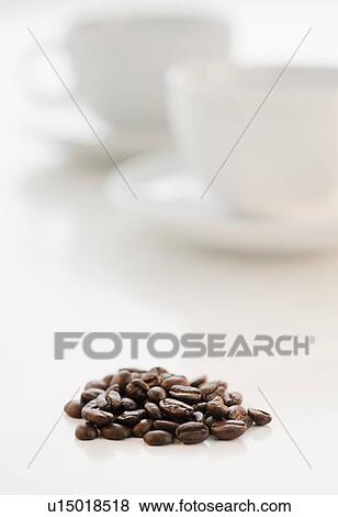 Stock Photo - Heap of coffee beans with coffee cups in background. Fotosearch