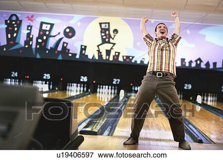 Stock Photo - Man standing in front of bowling alley and cheering. Fotosearch