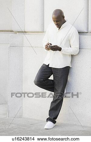 Picture - Man text messaging outside office building. Fotosearch