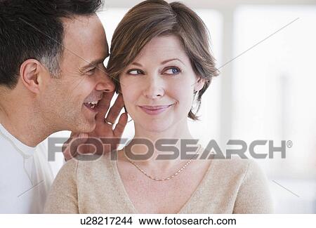 Picture - Man whispering to woman's ear. Fotosearch
