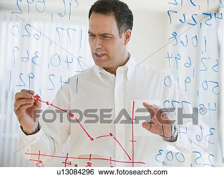 Stock Photograph - Mature businessman drawing line graph on transparent glass wall. Fotosearch