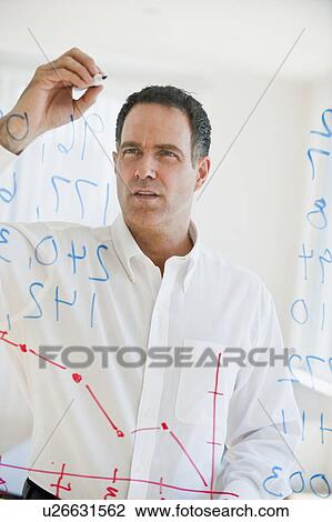 Stock Image - Mature businessman writing numbers on transparent glass wall. Fotosearch