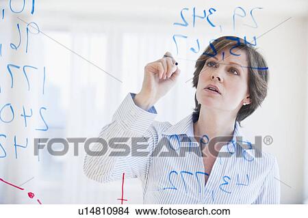 Picture - Mature businesswoman writing numbers on transparent glass wall. Fotosearch
