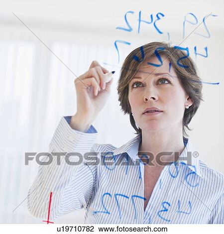 Stock Image - Mature businesswoman writing numbers on transparent glass wall. Fotosearch